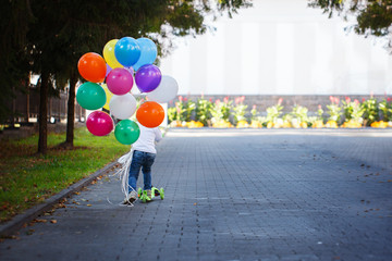 Happy boy with a bunch of colored balloonsriding a scooter. Back view
