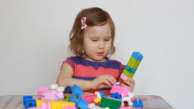 Little baby playing with colourful small blocks of a constructor. The child develops his thinking and motor skills. A sweet girl is busy building. Entertainment and games for children. Development and