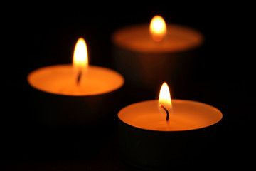 Many candle flames glowing in the dark.