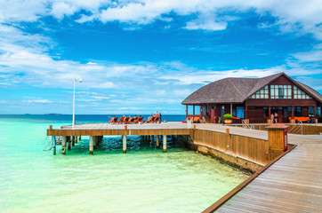 Wooden jetty with deckchairs nad bungalow on the background of the azure water of the Indian Ocean