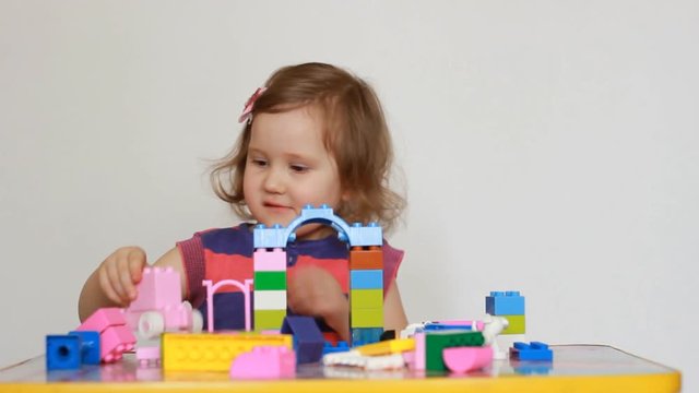 Little girl playing with colourful small blocks of a constructor. The child develops his thinking skills. Entertainment and games for children.