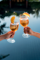 Concept picture of a couple holding glasses of cocktail and cheers by the swiming pool to celebrate...