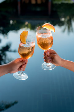 Concept picture of a couple holding glasses of cocktail and cheers by the swiming pool to celebrate their success.