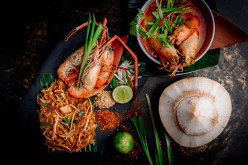 Concept pictures of famouse Thai dishes, Tom Yum Kung, Phad Thai and coconut. Beautiful presentation on black stone and black background.