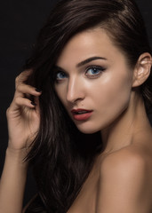 Portrait of a beautiful young girl with dark long hair and professional make-up on a black background.