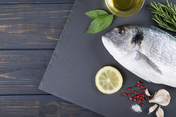 Raw fish dorado cooking and ingredients.  Dorado, lemon, tomato, herbs and spices. Top view on wood...