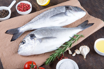 Raw fish dorado cooking and ingredients.  Dorado, lemon, tomato, herbs and spices. Top view on wood table