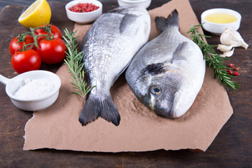 Raw fish dorado cooking and ingredients.  Dorado, lemon, tomato, herbs and spices. Top view on wood table