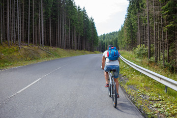 Young man with backpack cycling on road in mountains