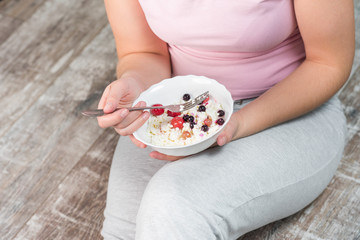 The girl is holding a plate of cottage cheese. Healthy eating concept. Cottage cheese with berries. Girl in home clothes. Proper nutrition. Diet. Plump girl. Health. Small depth of field.