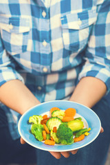 The girl holds a plate with vegetables. Healthy eating concept. A girl in jeans and a plaid shirt. Casual Style. Proper nutrition. Diet. Health. Vegetarian food. Vegans food. Toned image.