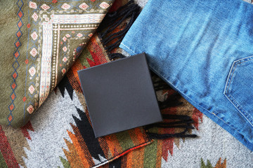 Black paper box on the background of patterned fabrics in boho style. Top view.