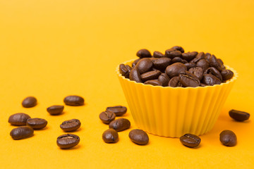 grains of coffee in a yellow container on a yellow background, a number of coffee grains scattered on a yellow surface