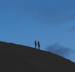Fashionable young people standing silhouetted on a hill at dusk