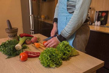 Man cooking healthy meal in the kitchen. Cooking healthy food at home. Male in kitchen preparing vegetables. Chef cuts the vegetables into a meal