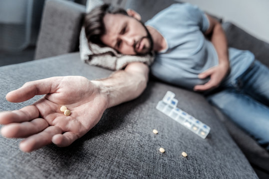 Strong sedatives. Selective focus of sedative pills being in a hand of a depressed sad man lying on the sofa