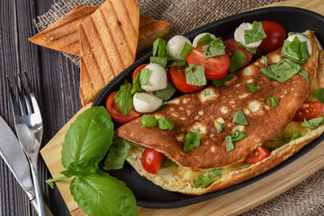 Vegetables omelette with tomatoes, basil, mozzarella, toast. Rustic
