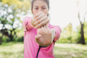 Close up of a young woman warm up her body by stretching her arms to be ready for exercising and do yoga in the park surrounded by nature and warm light afternoon sky. Outdoor workout exercise concept