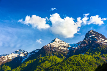 Surprisingly beautiful mountain range with melted snow and bright green forest at the foot. The helicopter flies over the valley with a waterfall. Caucasus mountains landscapes, Sochi, Russia.