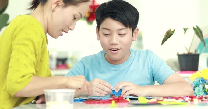 Happy asian family mother and son playing plastic block together .