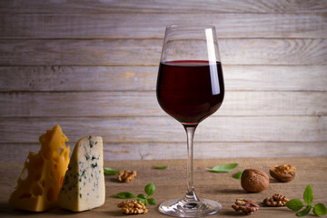 Red wine and cheese on wooden table background. Cheese appetizer selection or wine snack set. Glass and bottle of wine