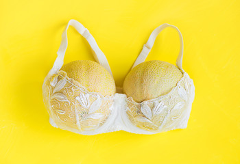 Breast enlargement concept, white bra with two melons on yellow background - obrazy, fototapety, plakaty