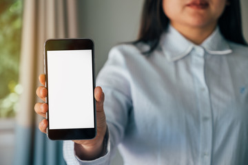 Mockup image of a beautiful woman holding and showing white mobile phone with blank white screen and smiley in office