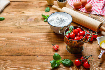 Italian cuisine  background, old kitchen tools and fresh food ingredients, Parmigiano, tomato, basil, olive oil, daugh ingredients, napkin on rustic wooden background. Top view
