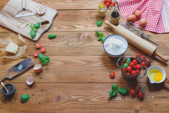 Italian cuisine  background, old kitchen tools and fresh food ingredients, Parmigiano, tomato, basil, olive oil, daugh ingredients, napkin on rustic wooden background. Top view