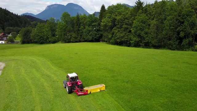 a red tractor harvesting a field of cow's grass in a farm in a small vilage in Tirol Austraia. drone footage