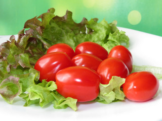 Red cherry tomatoes with green lettuce leaf on white plate