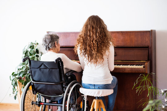 A Girl With Grandmother In Wheelchair Playing The Piano.