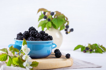 Fototapeta na wymiar Ripe blackberries with leaves in a blue ceramic bowl on white table