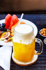 Tropical cocktail, mocktail, juice, refreshing drink from passion fruit in glass jar on table in cafe. Nuts, peanuts, olives, cappuccino coffee and fruits background.