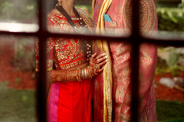 Look through the window at Indian newlyweds dressed in red suits and hugging in the garden