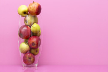 Ripe apples in transparent case against colorful background. Copy space