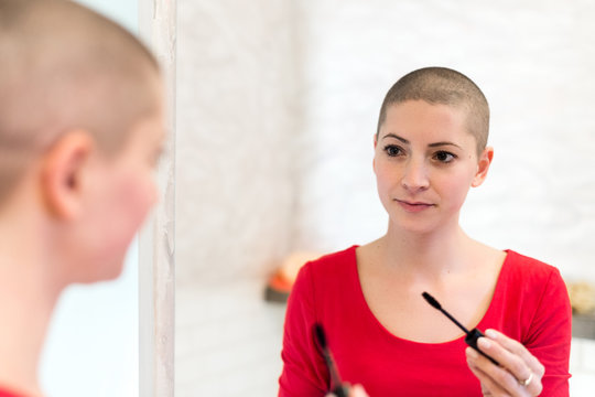 Young adult female cancer patient with gorgeous new short hair, looking in the mirror, smiling, applying mascara.