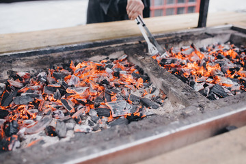In the barbecue grill the coals are lit, the cook interferes with the coals
