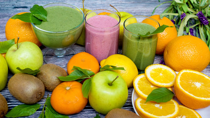 Fresh fruits and three glasses of smoothies on a wooden background