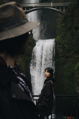 Man looks at an Asian woman standing before a waterfall somewhere in the mountains