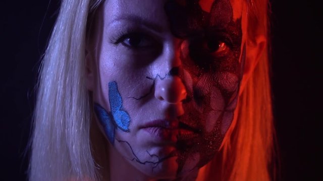 A girl with a bodypainting of blue butterflies on her face looks at her friend with hatred, slow motion