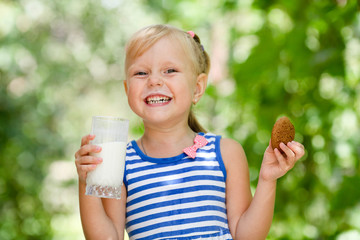 The joyful child drinks milk and eats cookies outdoors