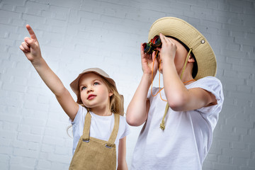 children in safari costumes and hats pointing and looking in binoculars - Powered by Adobe