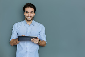 Modern device. Positive nice attractive man holding a tablet and smiling while using it