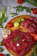 Still life of raw beef meat with vegetables on wooden plate over white background, top view, selective focus