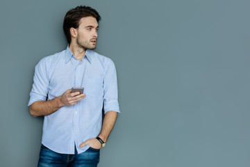 Digital device. Smart nice serious man standing and holding his smartphone while looking aside