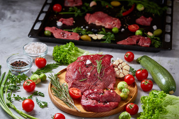 Still life of raw beef meat with vegetables on wooden plate over vintage background, top view, selective focus