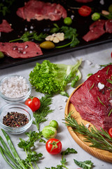 Still life of raw beef meat with vegetables on wooden plate over vintage background, top view, selective focus