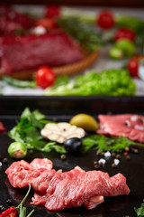 Still life of raw beef meat with vegetables on wooden plate over white background, top view, selective focus