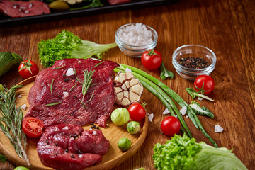 Still life of raw beef meat with vegetables on wooden plate over vintage background, top view, selective focus